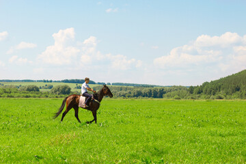 Boy riding a horse in the summer in the field. The village boy runs on horseback