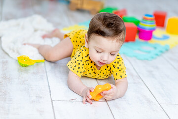 baby boy plays in the children's room in a yellow bodysuit with bright colorful toys