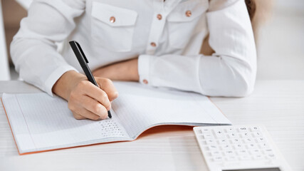 Fototapeta premium Cropped view of girl writing on notebook near calculator on blurred foreground.