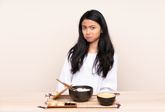 Teenager Asian Girl Eating Asian Food Isolated On Beige Background With Sad And Depressed Expression