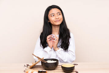 Teenager Asian girl eating asian food isolated on beige background scheming something