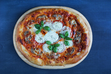 Oval pizza with mushrooms, mozzarella, tomatoes and basil on a wooden tray on a blue wooden table                        