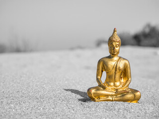 Small golden buddha statue or Buddharupa in the sand