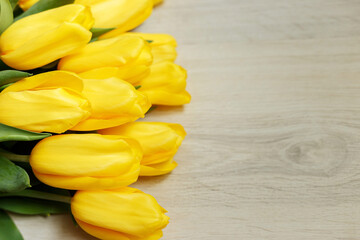 A bouquet of yellow tulips lies on a wooden background. Beautiful yellow flowers with green leaves. Background with flowers. Flowers for the holiday. Postcard with flowers with free space.