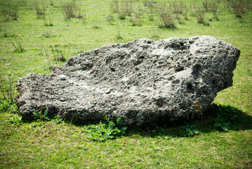 A large piece of concrete on the grass under the bright sunlight.