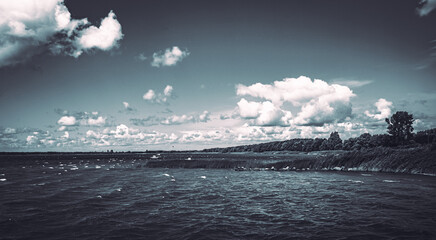 Düstere, surreale Aufnahme am Wasser mit schönem Wolkenband im Sommer am Badesee in monochrom...