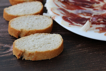 Plate of Iberian ham with slices of bread on wooden background