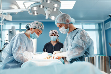 Doctors performing abdominoplasty surgery in the hospital. Focus on male plastic surgeon doing...