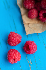 Group of seasonal summer berries on blue backgroound. Red raspberries from paper cornet