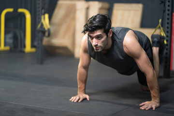Fototapeta premium Handsome adult Caucasian men push up with trx robe to do crossfit exercise inside of fitness gym to workout for firm abs muscle and good body health.