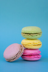 Vertical photo of group different colored french macarons on blue background. French dessert