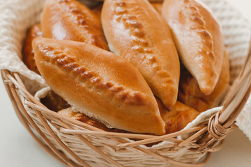 Baked pies in a wicker basket on a white table.