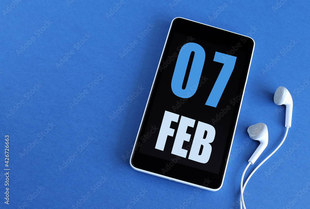 Wall mural february 7. 7 st day of the month, calendar date. smartphone and white headphones on a blue backgrou