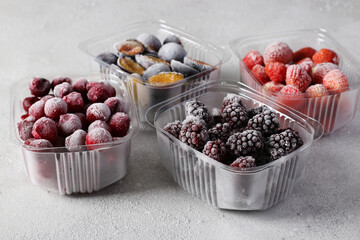 Frozen berries such as cherries, strawberries, plums and blackberries in the storage boxes on the concrete gray background