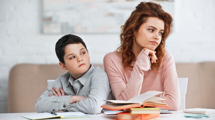 Displeased woman and son sitting near notebook and books at home.