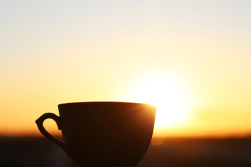 Silhouette of coffee cup on sunrise background, fresh start in the morning. Cozy atmosphere, city view from the window
