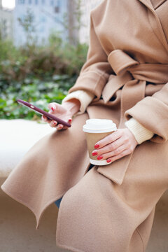 Woman is drinking speciality coffee on the street while having break. Close-up of hands with take away coffee. Reading news, e-mail, surfing the web
