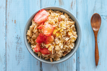Top view of oats porridge with hazelnuts and strawberry sorbet in ceramic bowl over blue wooden background. Healthy breakfast ideas.