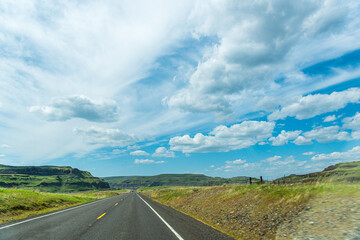 Travel-A Two-Lane Blacktop Road Approaching the Green-Carpeted Basalt Cliffs of the Columbia River Basin in Eastern Washington State