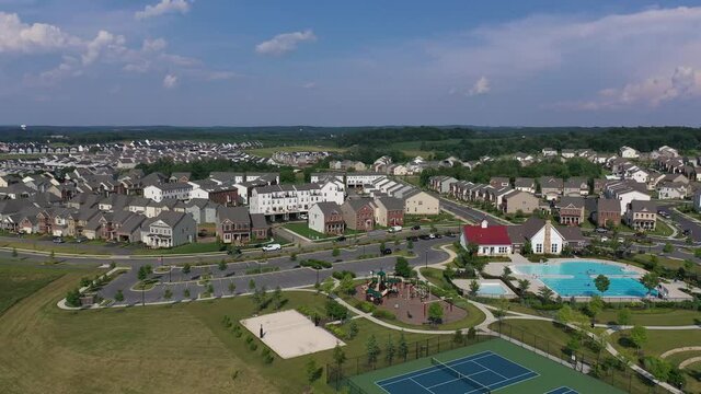 Circling above a modern upper middle class single family homes neighborhood street American real estate in a new town planned city, club house with tennis courts, playground and large community pool
