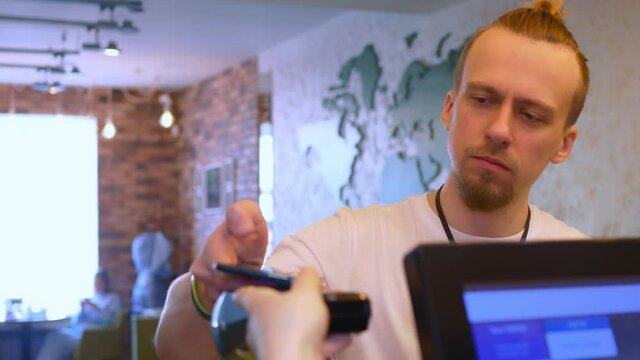 The cashier of the restaurant serves the visitor, giving him an acquiring terminal, the visitor makes a payment with a smartphone, uses the NSF payment. Small business. Close-up.