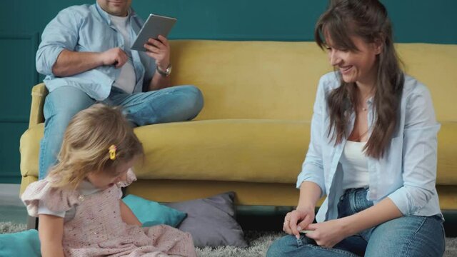 Mom is always there to help. Little girl playing with mother on the carpet, while her father works using a tablet. Spending time together at home.