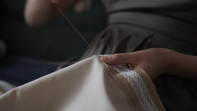 4K Closeup view of female hands sewing  jute linen stripe to beige cotton cloth. Boho rustic  style. Young woman sew tablecloth. Manual sewing.Handmade concept. Daylight. Hobby time.