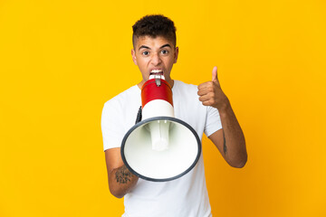 Young brazilian man isolated on yellow background shouting through a megaphone to announce...
