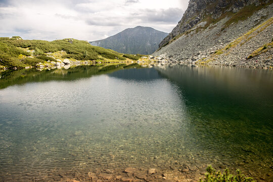A crystal clear mountain lake with green grass and mountains around and cloudy sky, Rohace, Rohacske plesa, Slovakia
