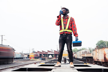 African machine engineer technician wearing a helmet, groves and safety vest is using a wrench to...