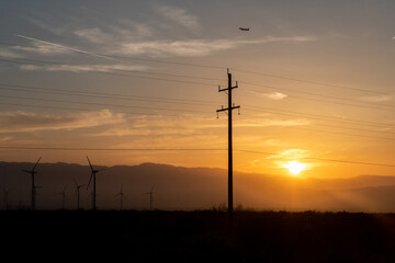 Sunrise in the desert with power lines and wind turbines.