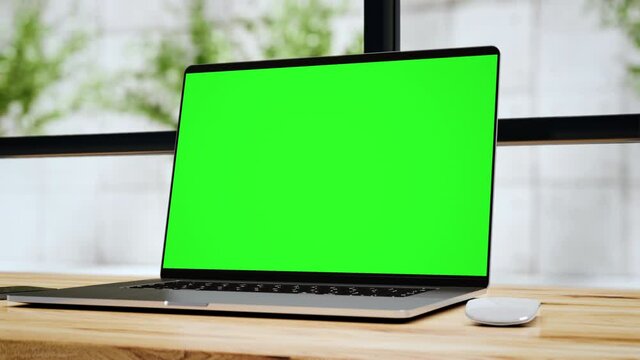 Laptop with blank green screen in office interior. Smooth camera movement around the object with a bokeh background. Home interior or office, 4k 24fps UHD