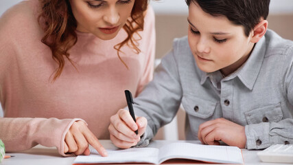 Boy writing on notebook near mother pointing with finger at home.