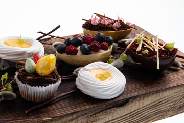 Selection of different sweet cupcakes, cookies and filled chocolate eggs on wooden board
