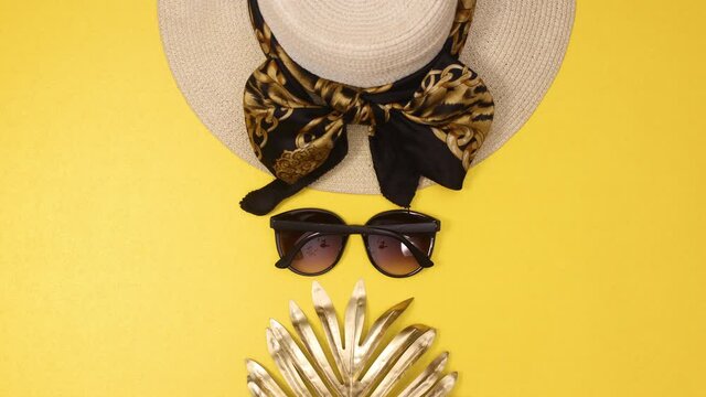 Glamourous beach hat and sunglasses and gold palm leaf appear on summer yellow background. Stop motion flat lay