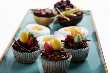Selection of different sweet cupcakes, cookies and filled chocolate eggs on handmade ocean plate
