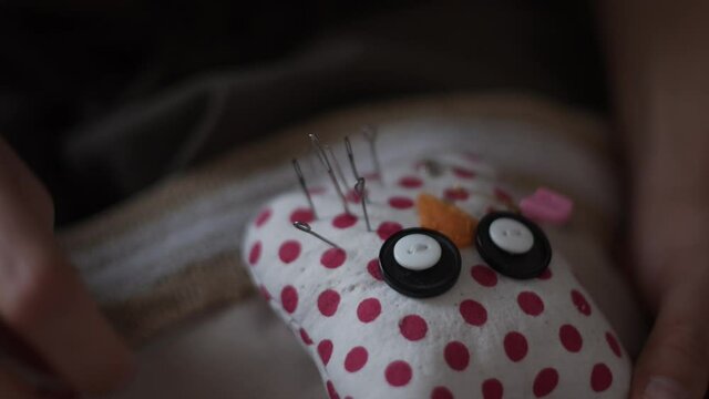 4K Close-up view of female hands inserting pins into pin cushion in shape of owl in polka dots which many pins and needles for embroidery and sewing are stuck in. Handmade concept.