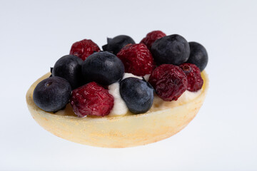 White chocolate egg filled with passion fruit mousse decorated with dried cranberries and fresh blueberries isolated on white