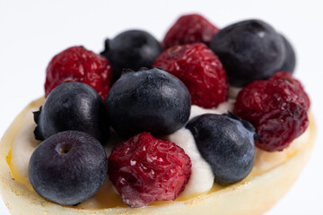 White chocolate egg filled with passion fruit mousse decorated with dried cranberries and fresh blueberries isolated on white