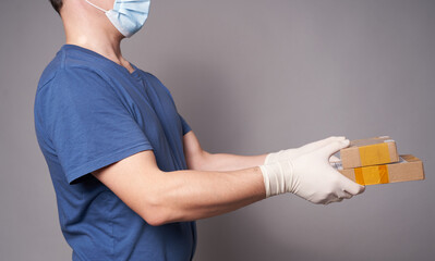 Hand of a white man in a medical mask and rubber gloves with two parcels on a gray background. Fast and safe delivery.