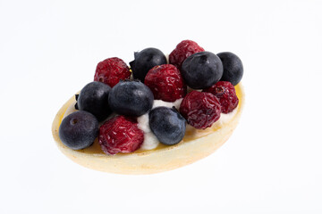 White chocolate egg filled with passion fruit mousse decorated with dried cranberries and fresh blueberries isolated on white