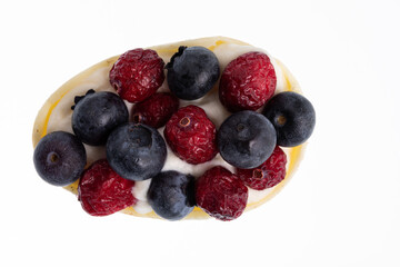 White chocolate egg filled with passion fruit mousse decorated with dried cranberries and fresh blueberries isolated on white