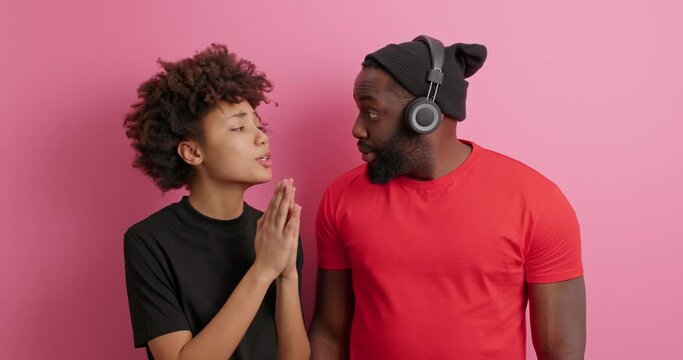 Culry haired woman holds hands in pleading gesture asks boyfriend for something has pleading expression needs help. Afro American guy in red t shirt receieves apologise from wife. I am sorry