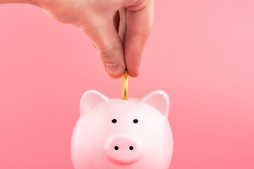 Pink piggy Bank and a man's hand puts down a coin on a pink background. Online business shopping concept