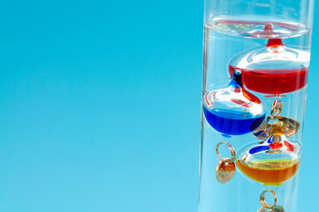Temperature measurement instruments, educational tools, meteorology concept with Galileo thermometer made of coloured glass balls in a water filled cylinder isolated on blue background with copy space