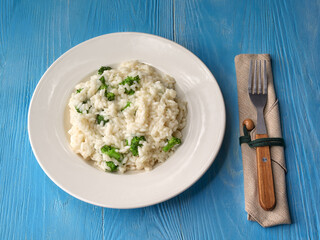 risotto with broccoli on white plate with rustic fork and served on light blue rustic table