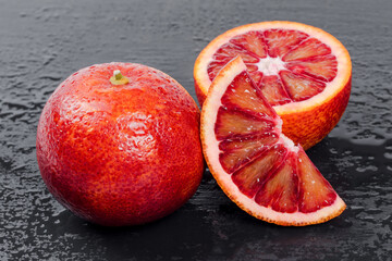 Bloody oranges whole and cut in half on black slate board with water drops. Red sicilian orange...