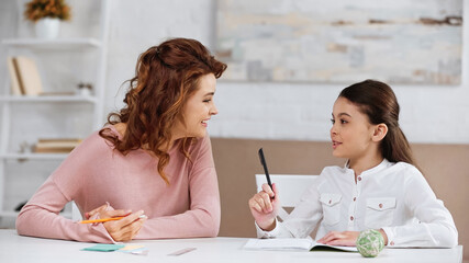 Smiling mother supporting daughter with homework at table.