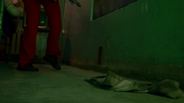 Close-up of the legs of a clown in red pants indoors throwing clothes on the floor