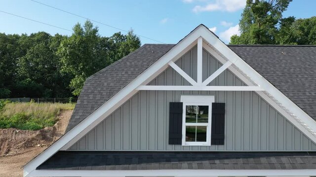 Horizontal flight along a triangle shape decorative gable with colonial white soffit and fascia on a gray horizontal vinyl siding modern American estate home with cloudy blue sky